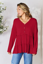 Woman wearing a red tiered long sleeve blouse with V-neck and buttons, paired with blue jeans.