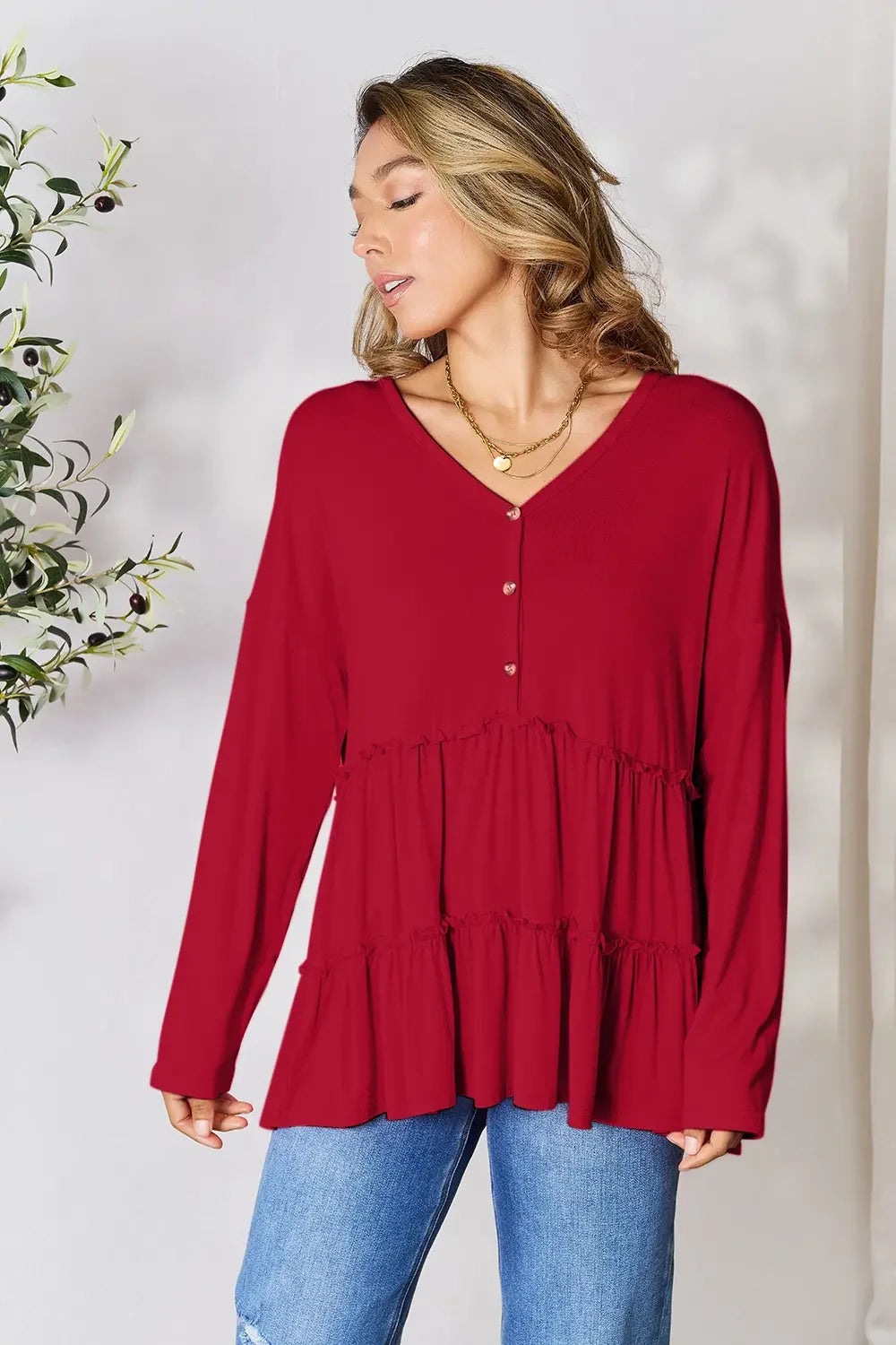 Woman wearing a red tiered long sleeve blouse with V-neck and buttons, paired with blue jeans.