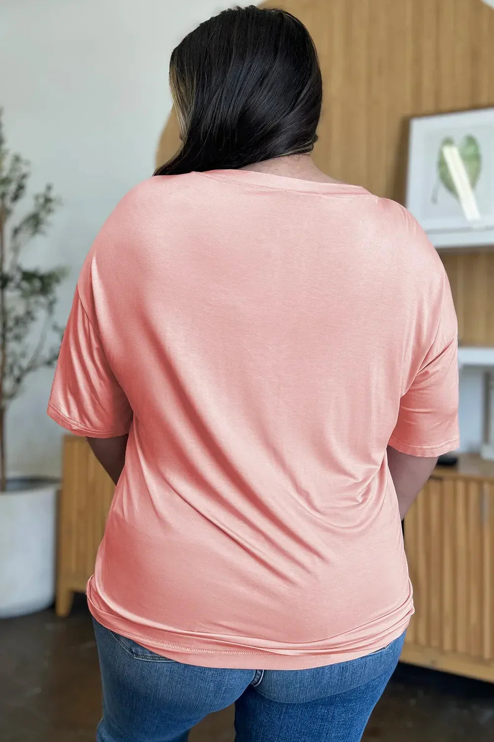 Woman wearing a peach short sleeve top and blue jeans, seen from the back indoors