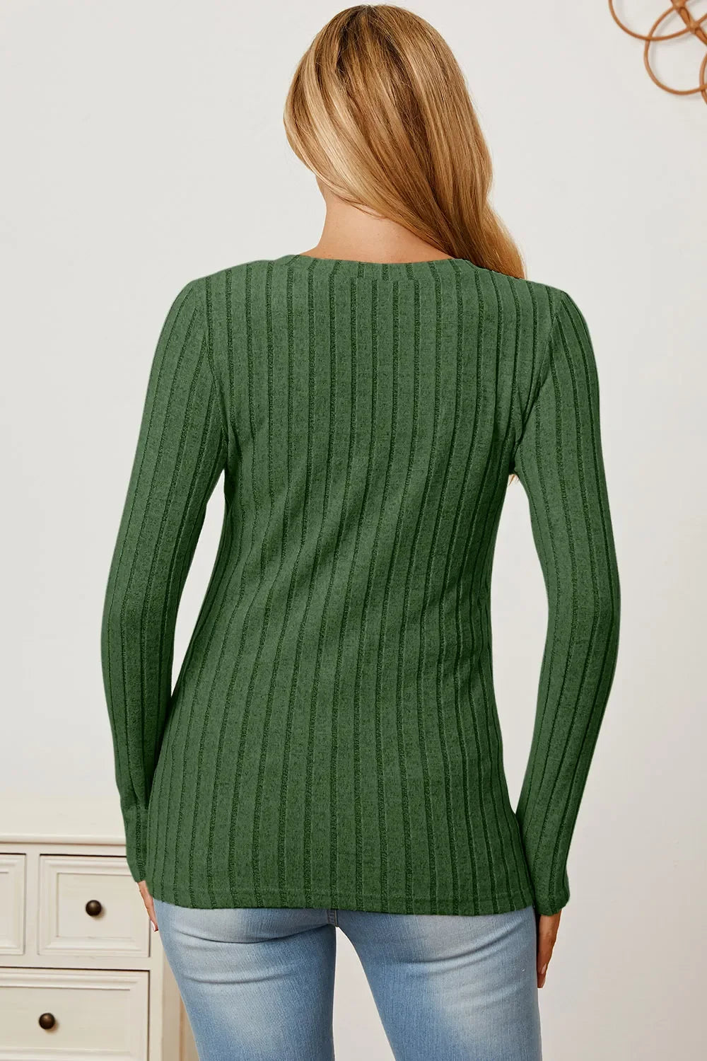 Woman wearing a green ribbed knit sweater with long sleeves and light blue jeans, back view