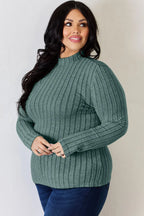 Woman wearing a green ribbed long sleeve sweater with mock neck and blue jeans