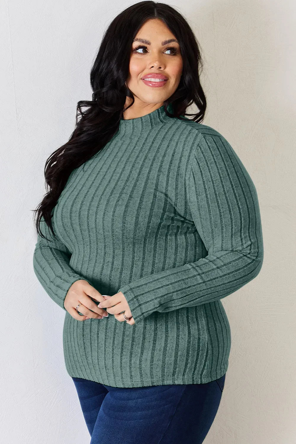 Woman wearing a green ribbed long sleeve sweater with mock neck and blue jeans