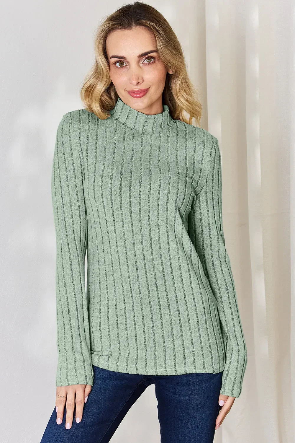 Woman wearing a light green ribbed knit mock neck sweater with long sleeves and blue jeans