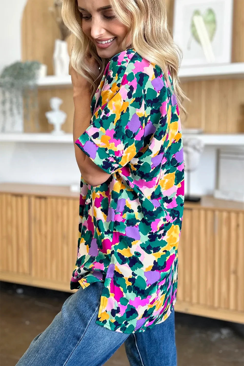 Woman wearing colorful abstract print short sleeve top and blue jeans indoors