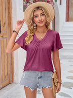 Woman in casual summer outfit with mauve top, denim shorts, straw hat and clutch outdoors