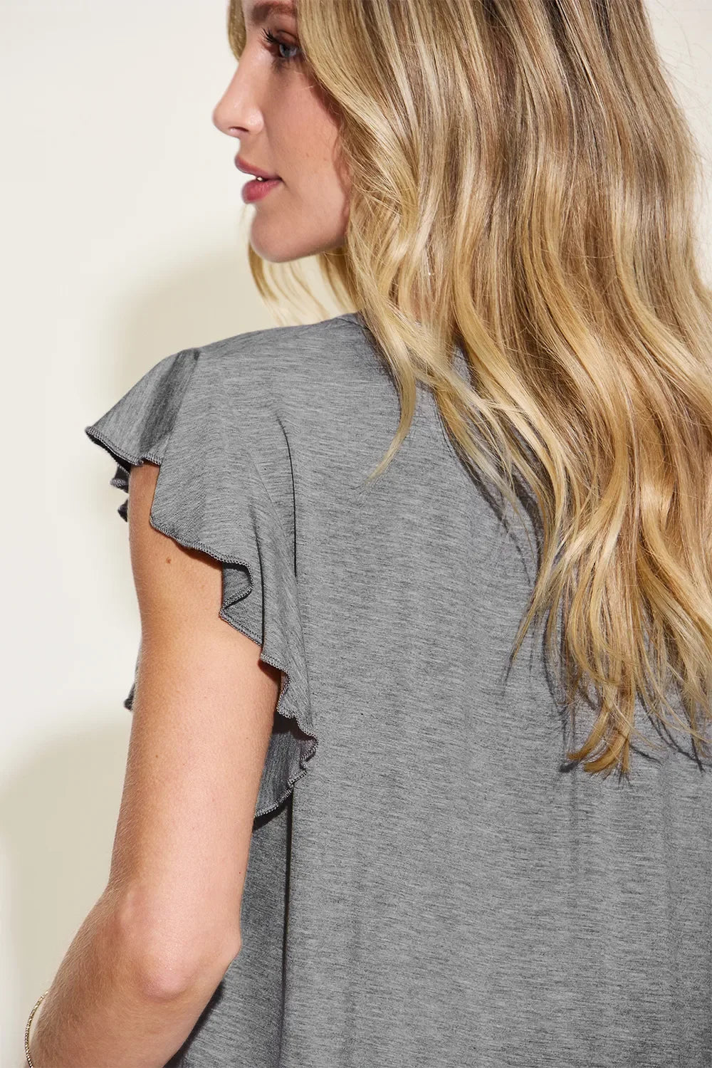Woman wearing a grey flutter sleeve top, side view, casual fashion outfit
