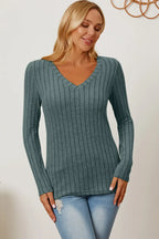 Woman wearing a gray ribbed V-neck long sleeve sweater and light blue jeans