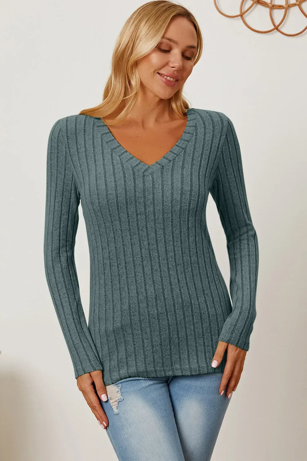 Woman wearing a gray ribbed V-neck long sleeve sweater and light blue jeans