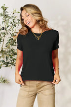 Woman wearing a black short sleeve t-shirt and beige pants with layered gold necklaces