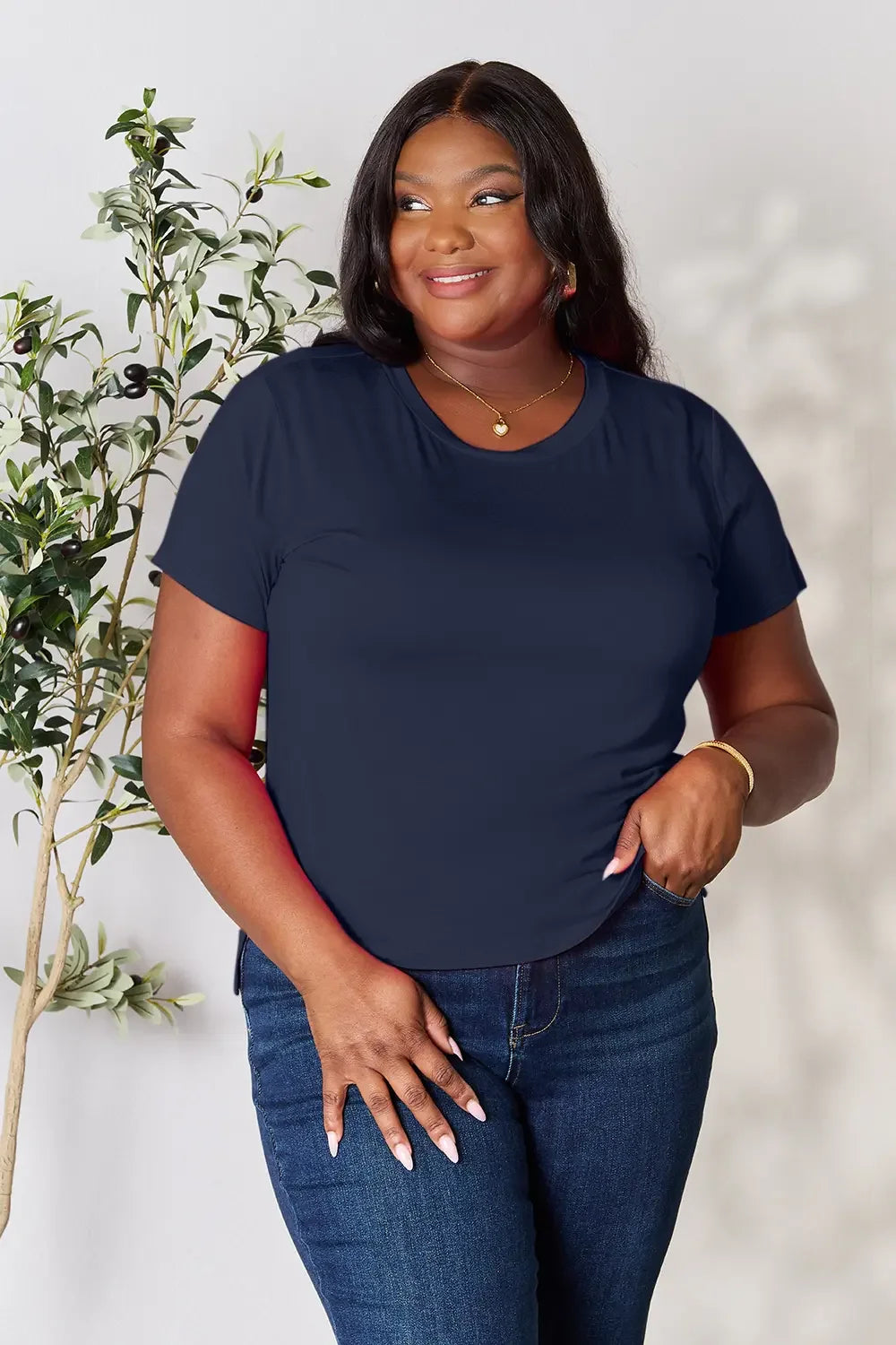 Woman wearing navy blue short-sleeve t-shirt and jeans, standing near indoor plant
