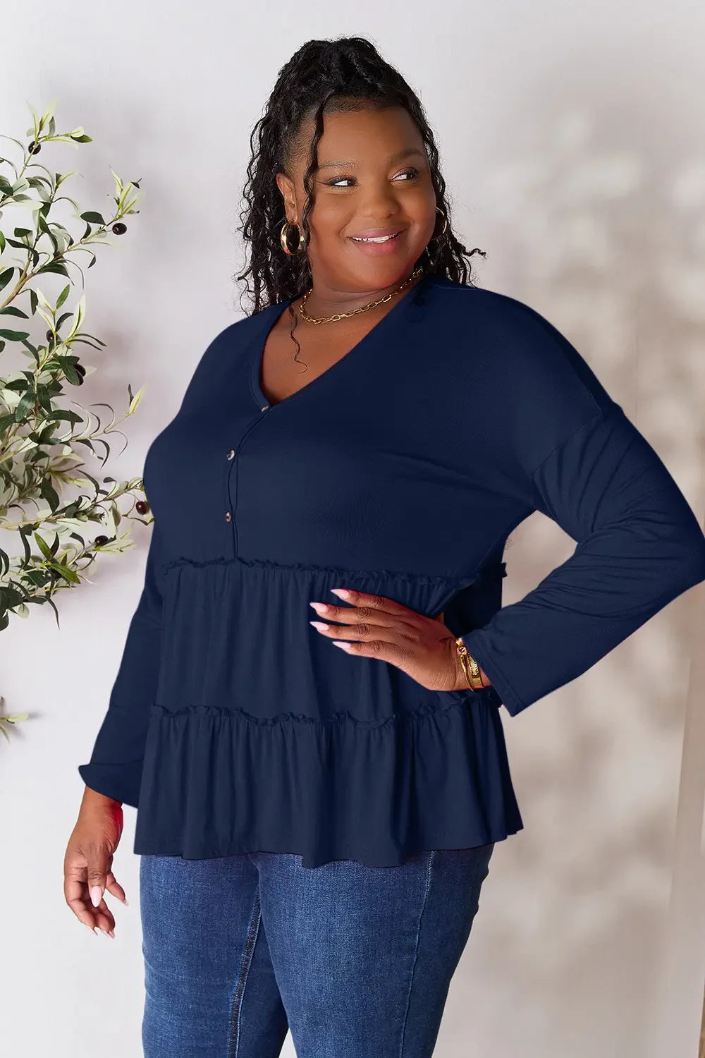 Plus size woman in navy long sleeve ruffle top and blue jeans, smiling indoors