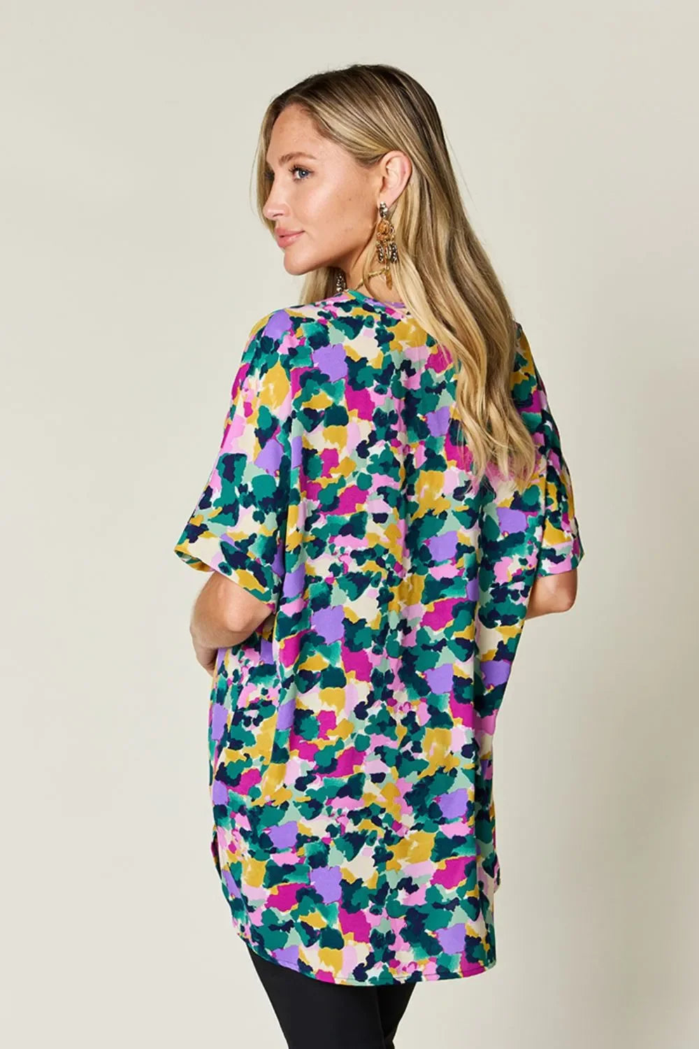 Woman wearing a colorful abstract print short sleeve blouse, facing away.