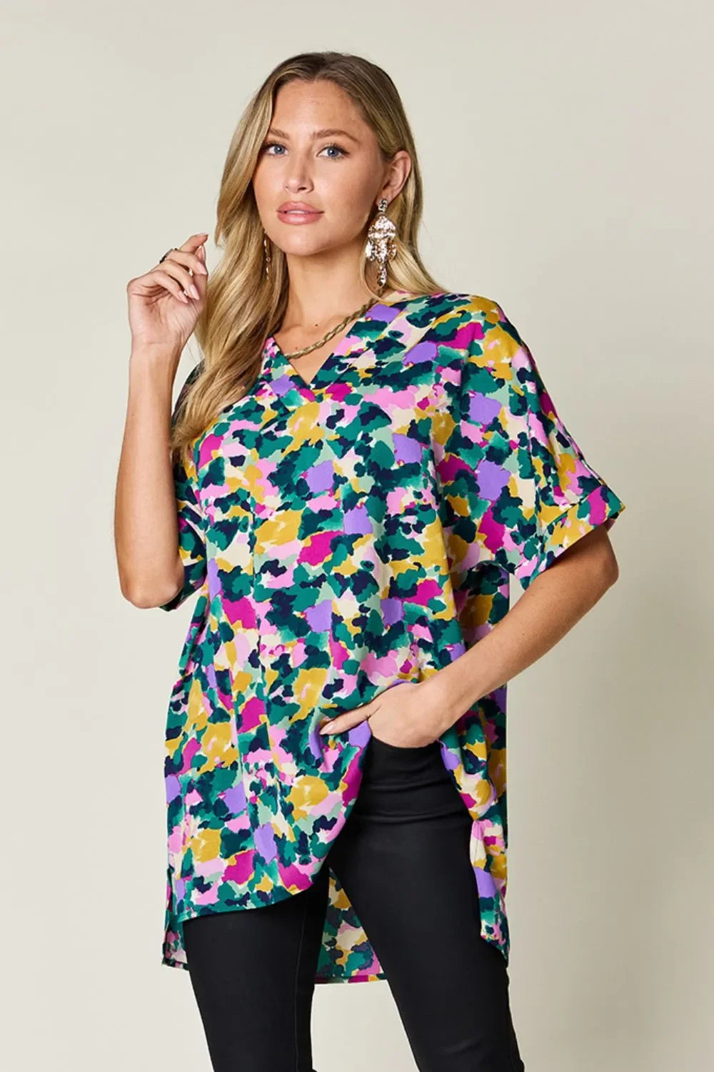 Woman wearing a colorful abstract print tunic top with black pants, accessorized with statement earrings.