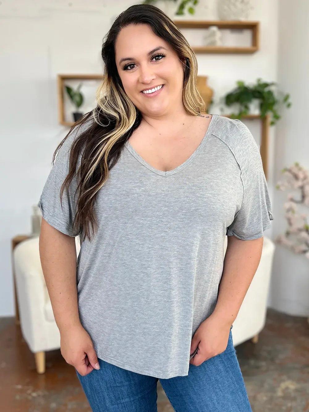Smiling woman wearing a casual gray V-neck t-shirt and blue jeans indoors
