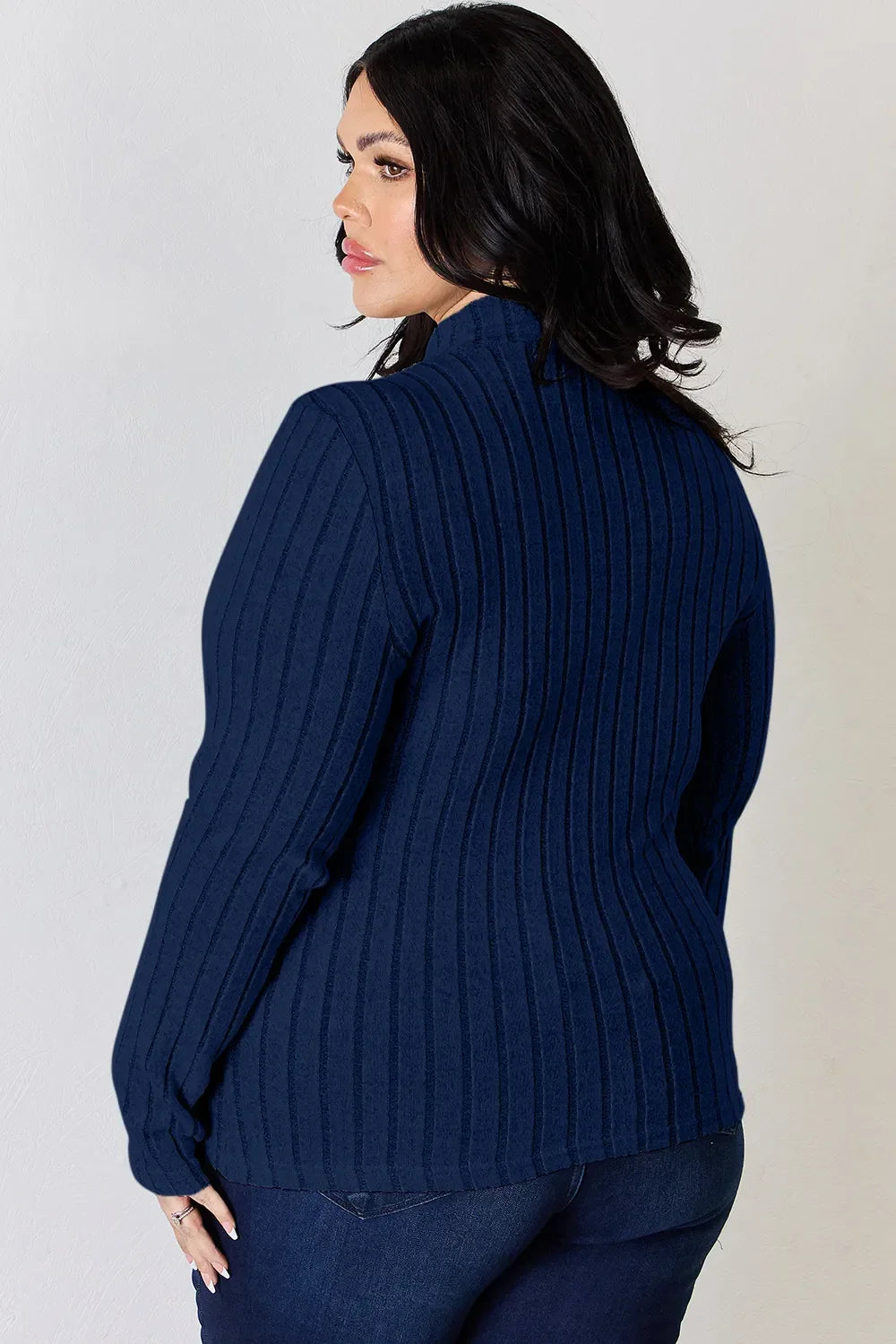 Woman wearing a navy ribbed sweater with long sleeves and dark blue jeans