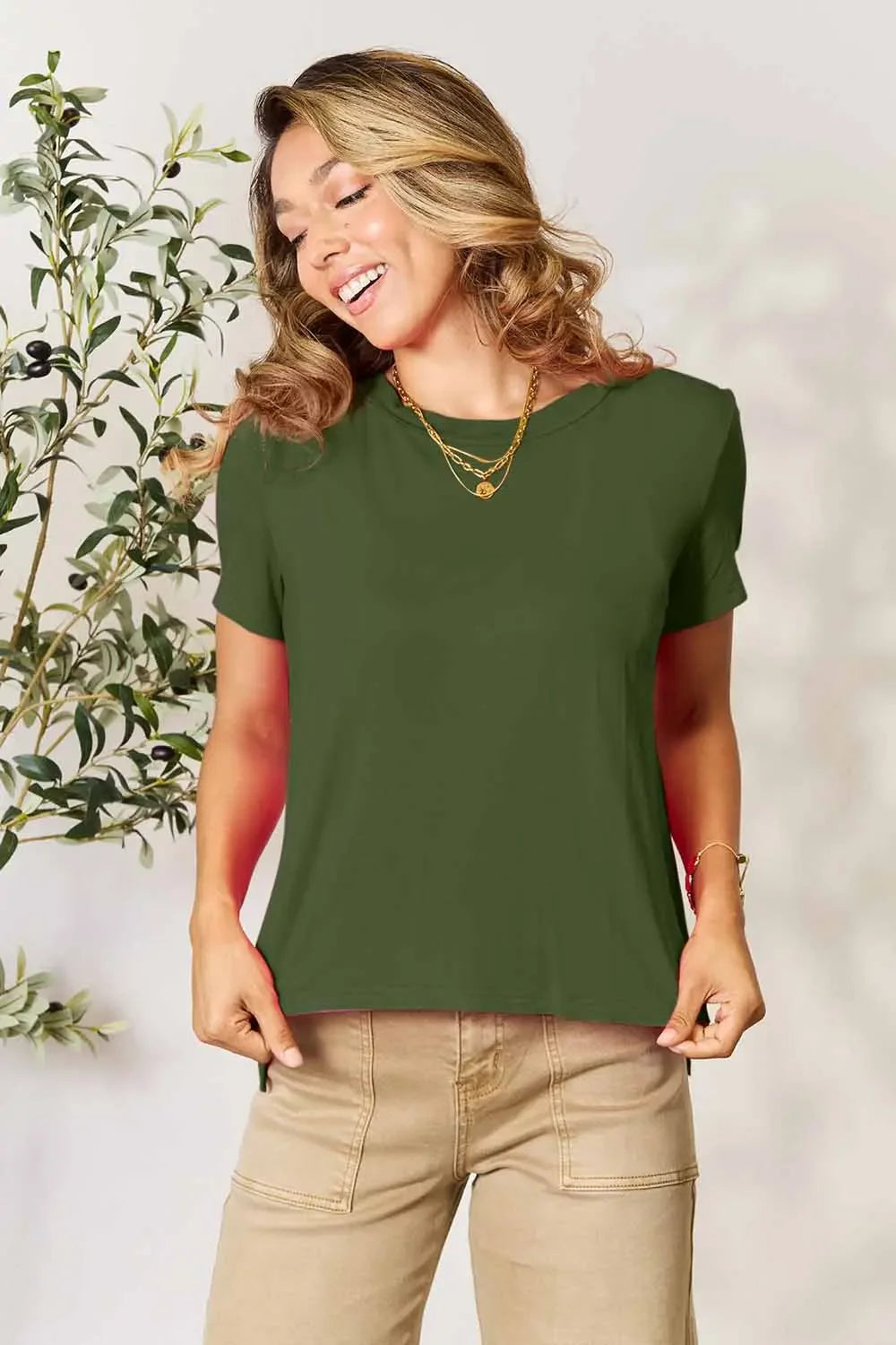 Woman modeling casual olive green short sleeve top with beige pants and gold layered necklaces