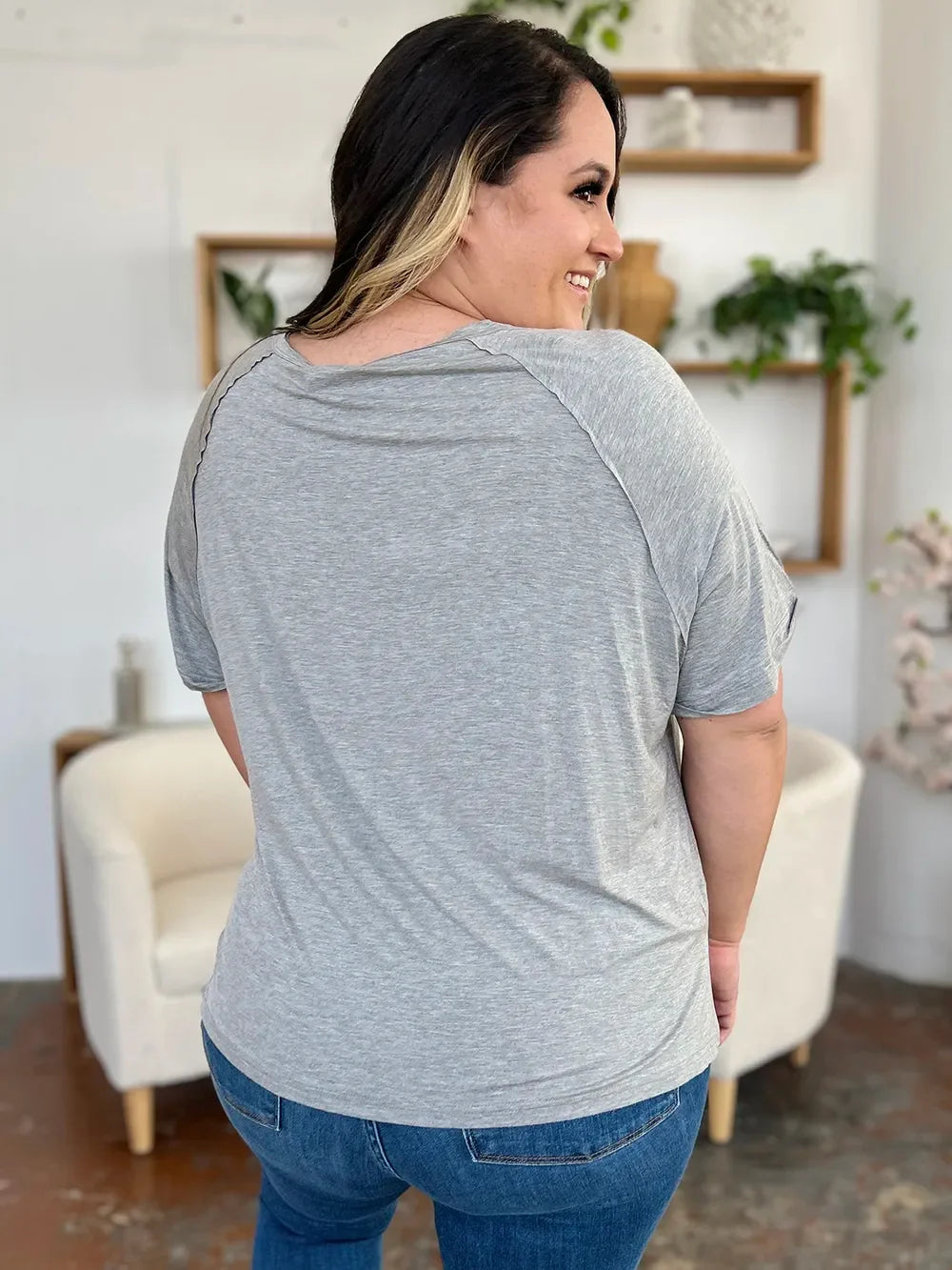 Woman in gray short sleeve t-shirt and blue jeans, indoor casual outfit, back view