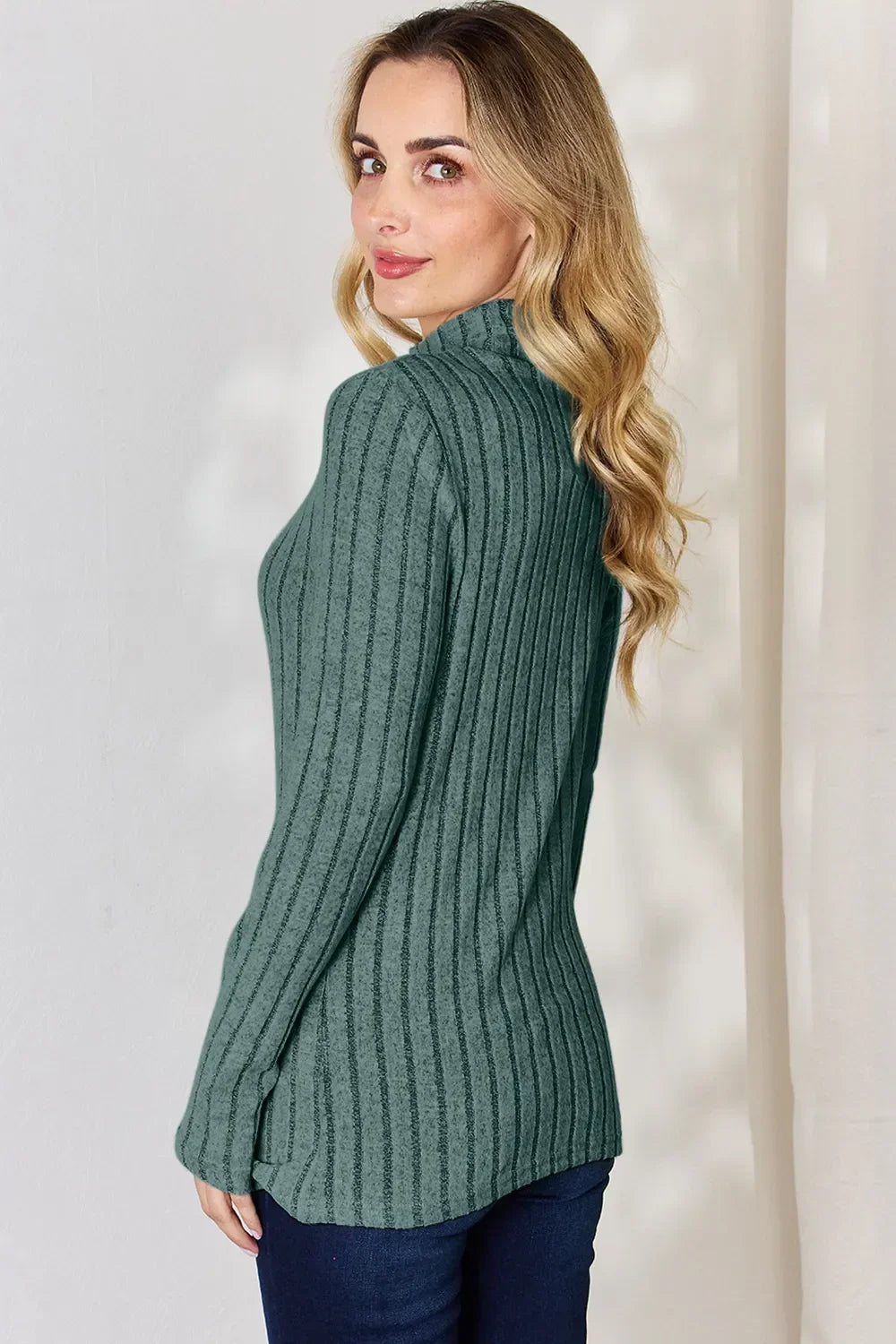 Woman in green ribbed long sleeve sweater and jeans, side pose, casual fashion
