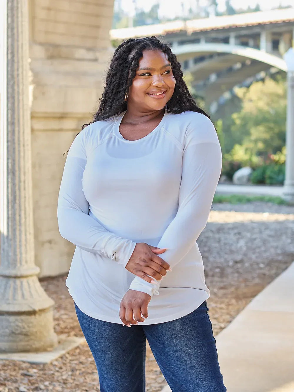Woman in a long sleeve light blue top and jeans smiling outdoors