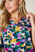 Woman wearing abstract multicolor print blouse, gold statement earrings, and gold necklace