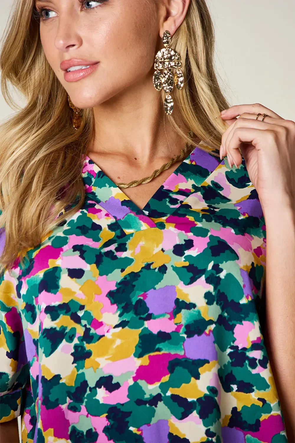 Woman wearing abstract multicolor print blouse, gold statement earrings, and gold necklace
