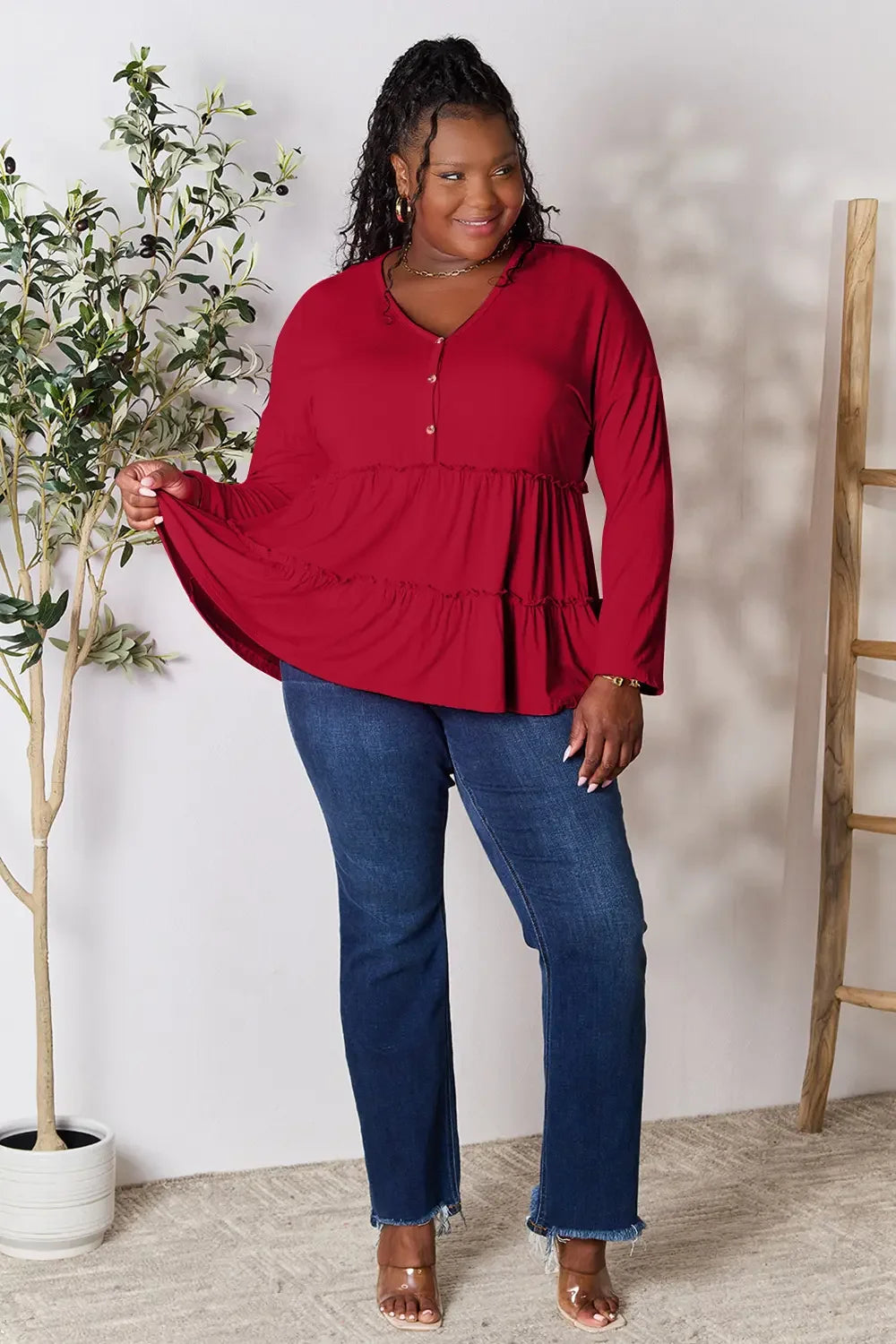 Woman wearing a long sleeve red tiered tunic top with blue jeans and clear sandals