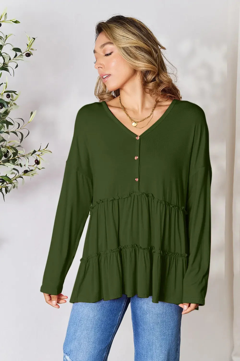 Woman wearing olive green ruffle long sleeve tunic top with jeans, layered gold necklace