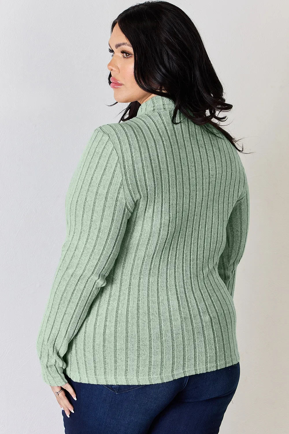 Woman wearing light green ribbed knit sweater and dark blue jeans, back view