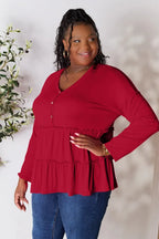 Smiling woman wearing a red tiered long sleeve blouse and blue jeans