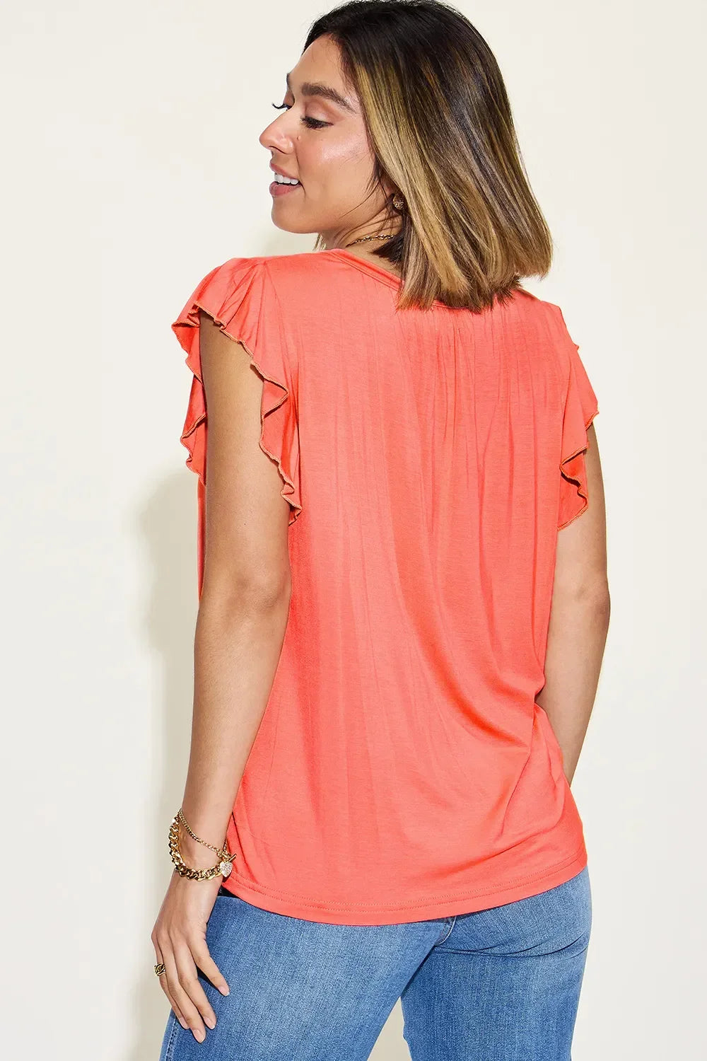 Woman wearing coral ruffle-sleeve top and blue jeans, back view, casual fashion