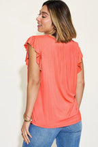 Woman wearing coral ruffle-sleeve top and blue jeans, back view, casual fashion