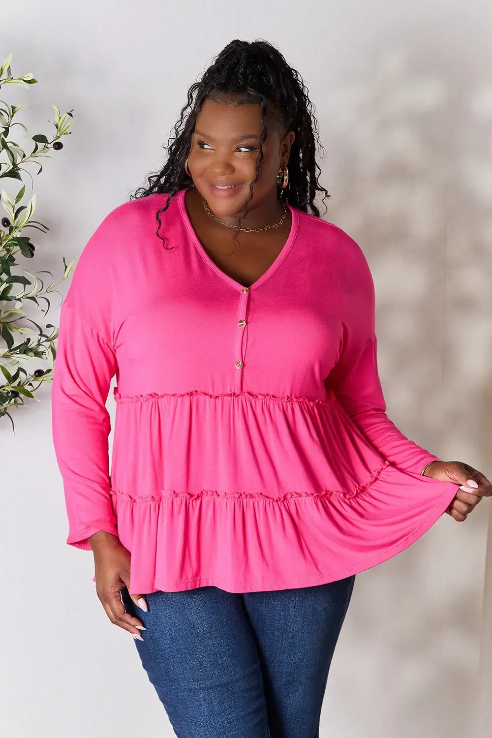 Woman modeling a bright pink long sleeve tiered blouse with gold buttons and blue jeans