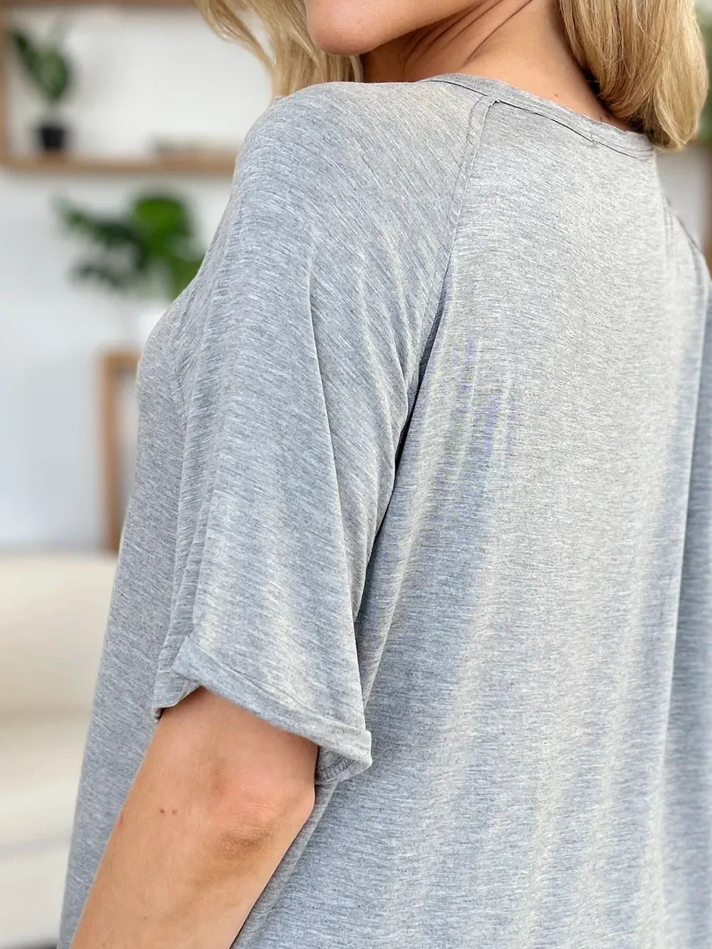 Close-up of woman wearing a loose heather gray short sleeve top in a casual indoor setting