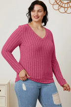 Woman wearing a pink ribbed V-neck long sleeve sweater and distressed blue jeans