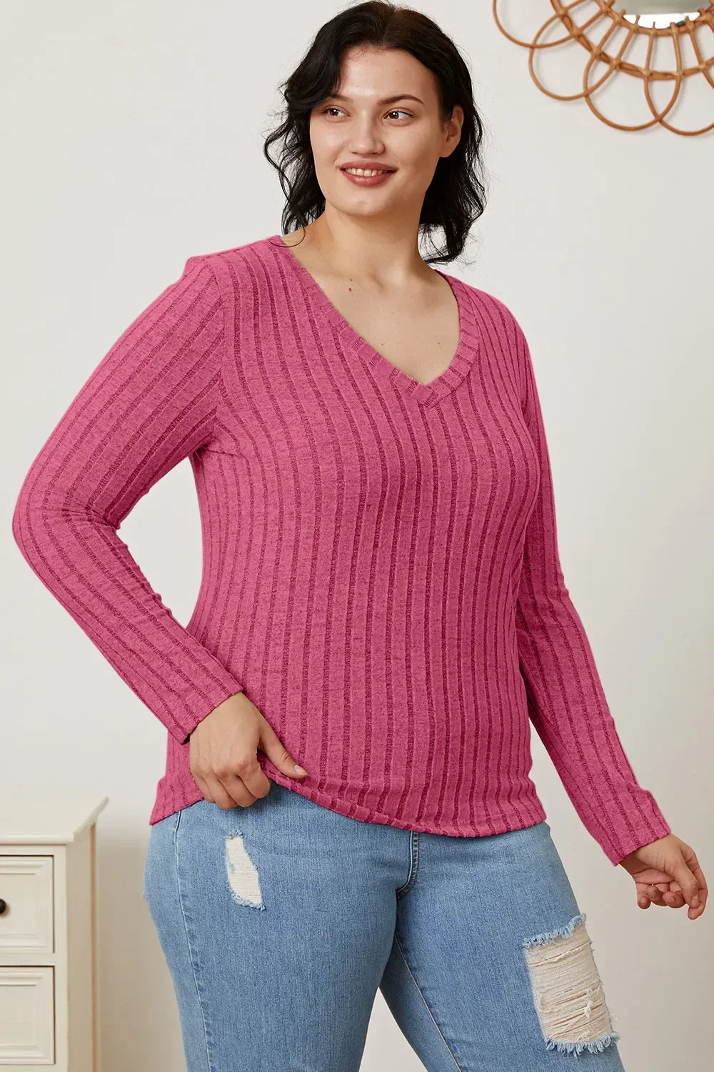 Woman wearing a pink ribbed V-neck long sleeve sweater and distressed blue jeans