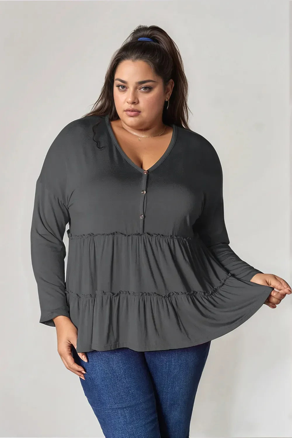Plus size woman wearing a dark tiered long sleeve blouse and blue jeans