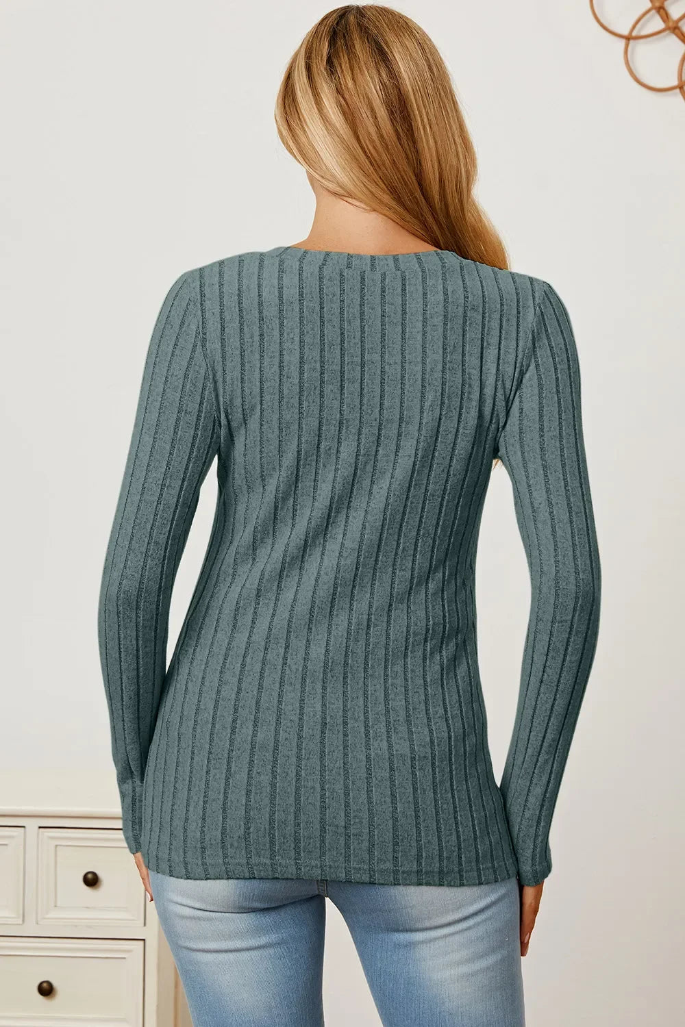 Woman in blue ribbed long sleeve sweater and light wash jeans, back view