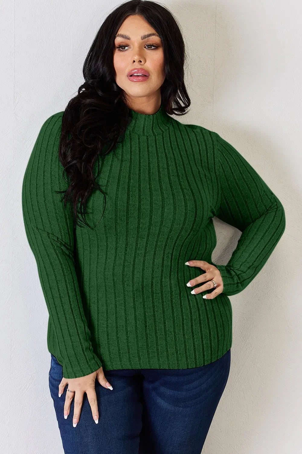 Woman wearing a green ribbed knit long sleeve sweater and dark blue jeans