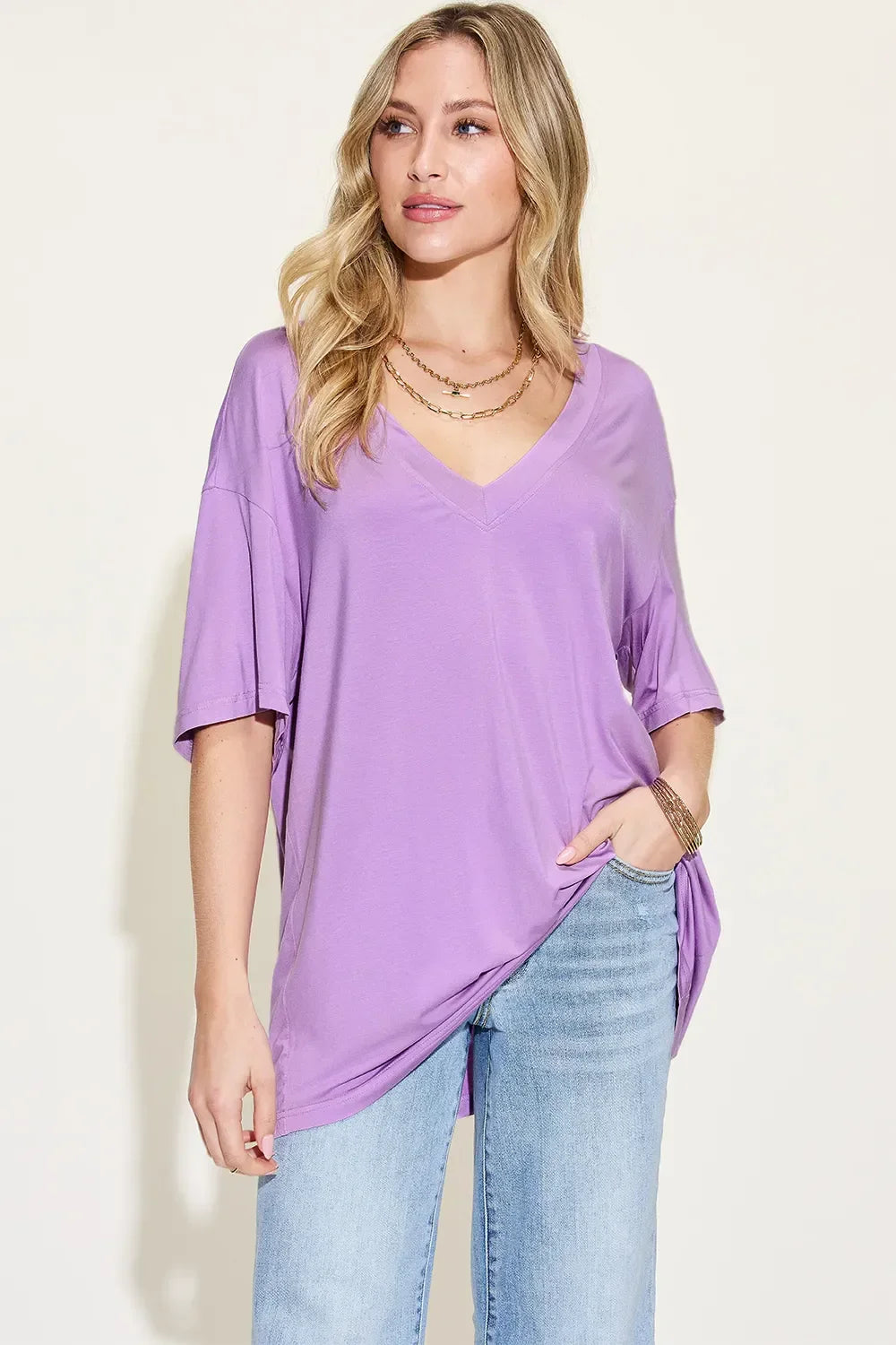 Woman wearing loose lavender V-neck t-shirt and light blue jeans on light background