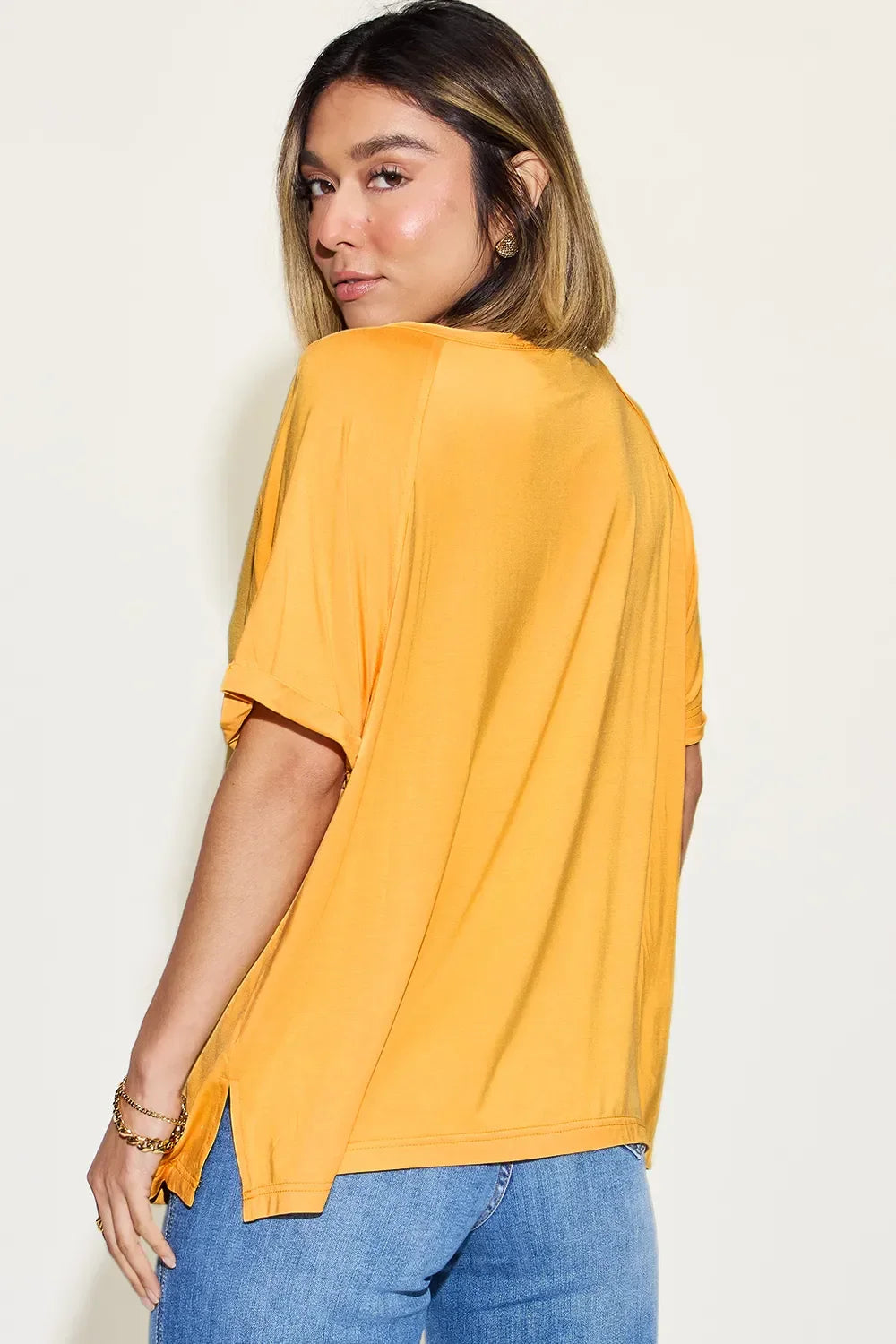 Woman in casual yellow short sleeve top and blue jeans, back view, cream background