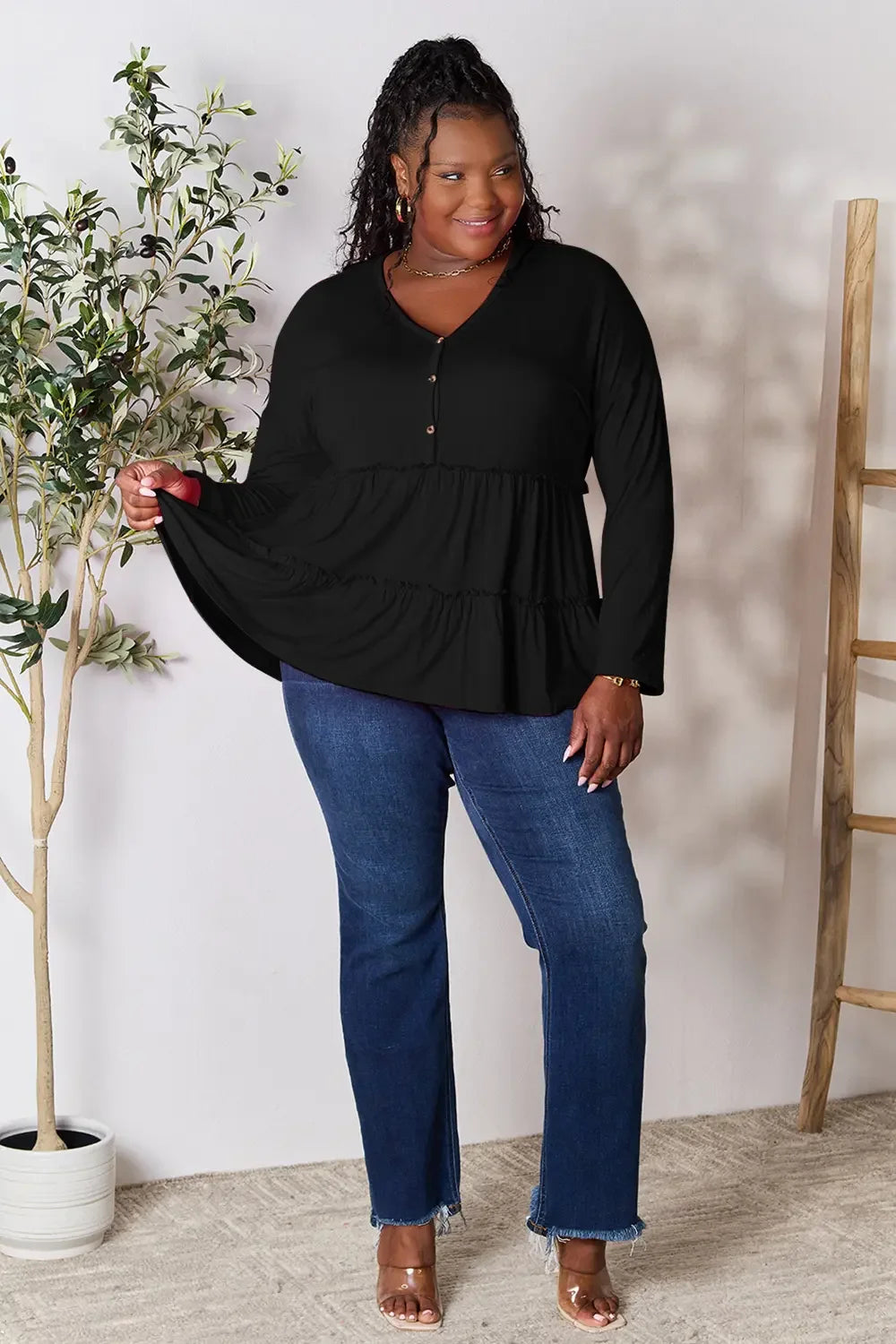 Woman in a black tiered tunic top and blue jeans posing indoors, plus size fashion
