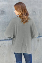 Woman in casual grey long sleeve top and blue jeans standing against concrete wall