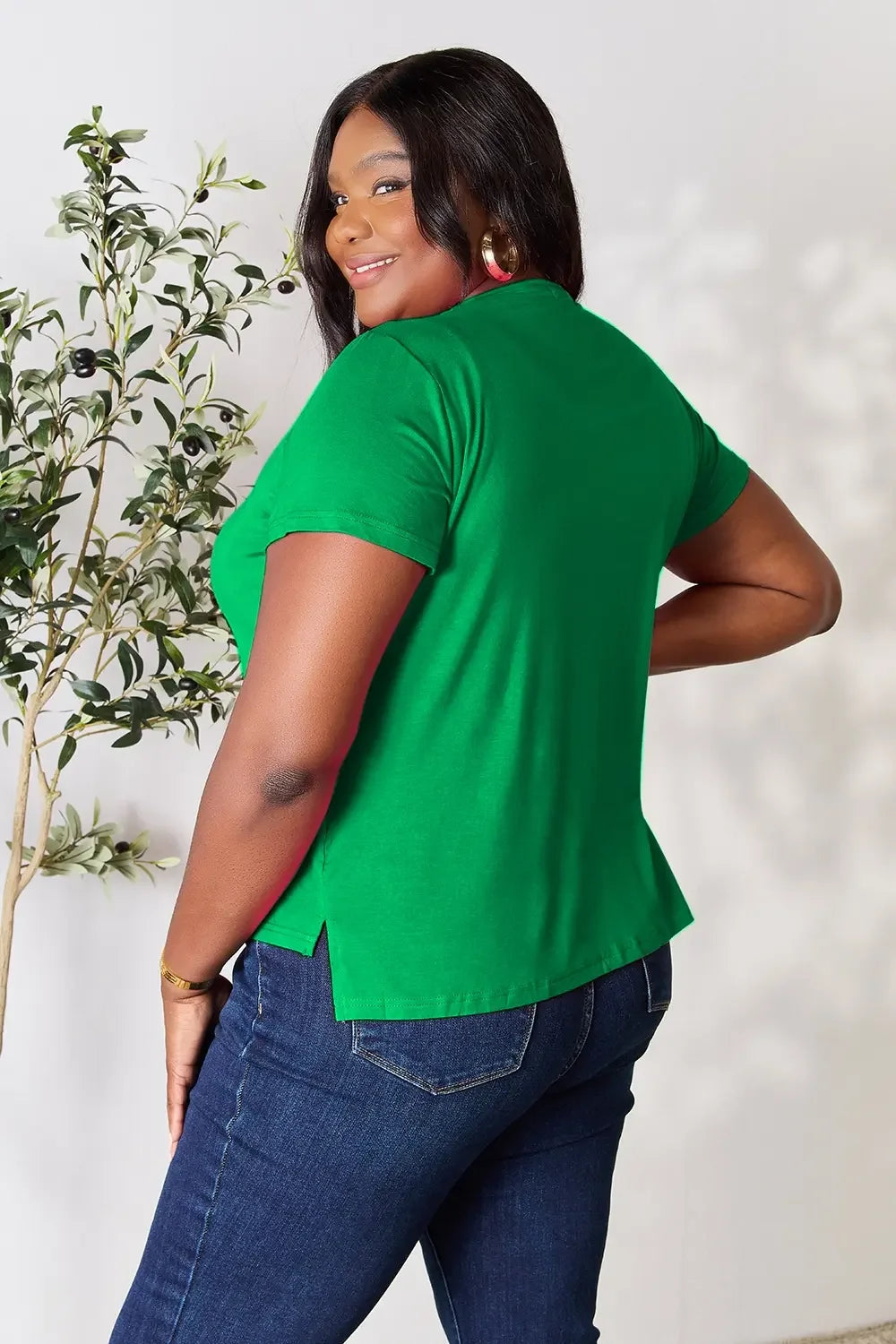 Woman in a green short-sleeve top and blue jeans smiling, casual outfit