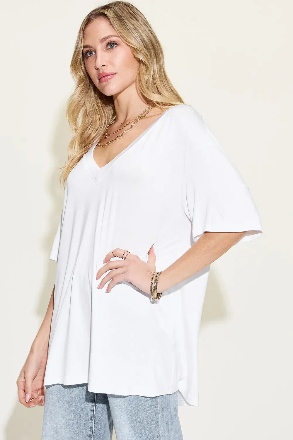 Woman wearing a loose white V-neck t-shirt and light wash jeans, styled with gold jewelry