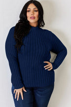 Woman wearing a navy blue ribbed knit sweater and dark jeans, standing indoors.