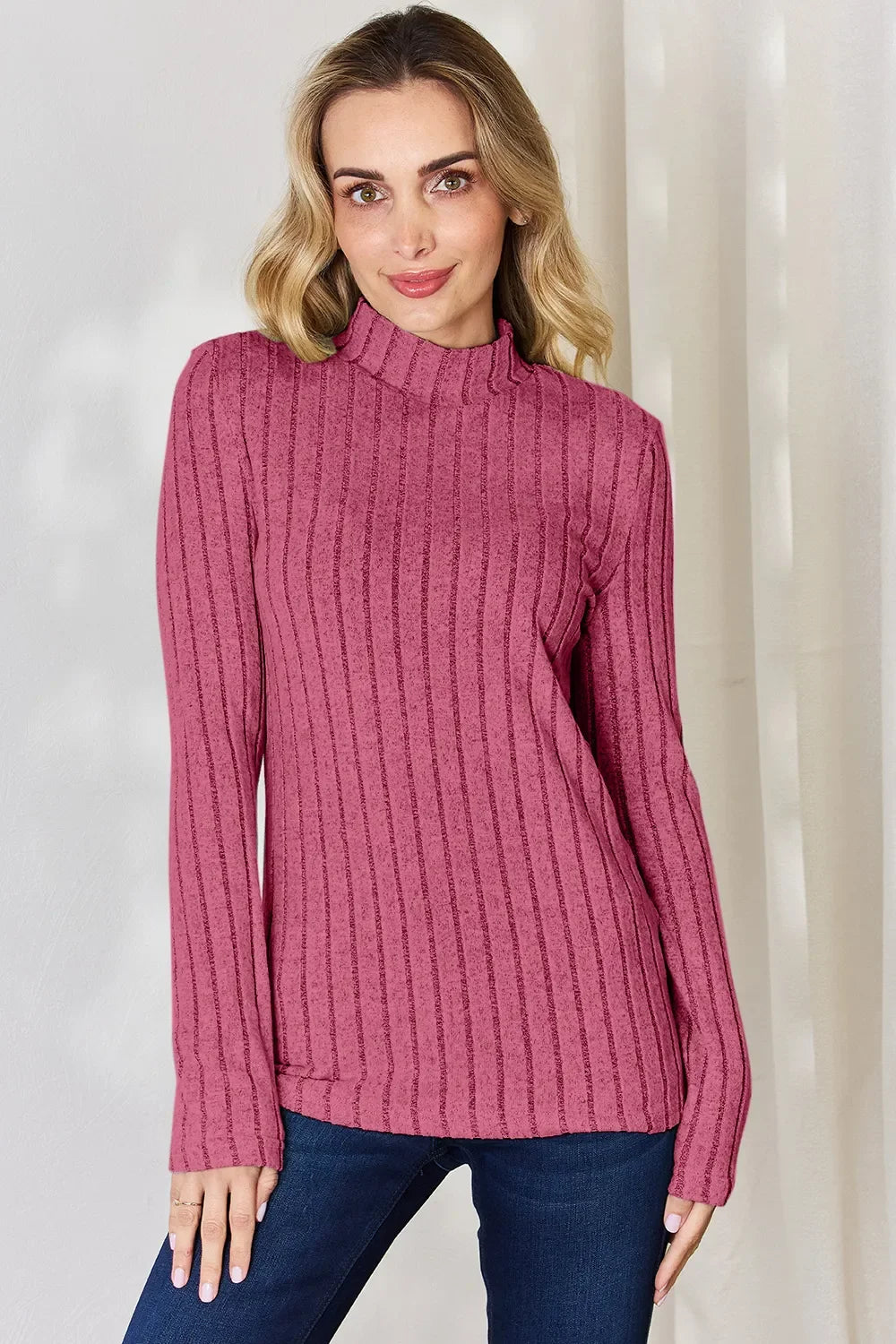 Woman wearing a pink ribbed long sleeve mock neck sweater with dark blue jeans