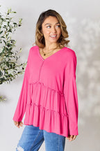 Woman wearing a bright pink long-sleeve ruffled blouse with blue ripped jeans