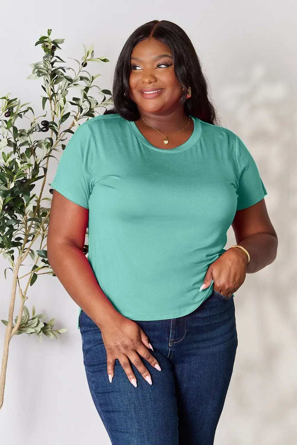 Woman in teal short sleeve t-shirt and blue jeans, smiling, casual fashion outfit