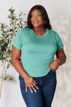 Woman in teal short sleeve t-shirt and blue jeans, smiling, casual fashion outfit