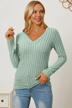Woman wearing a light green ribbed knit V-neck sweater with long sleeves and blue jeans